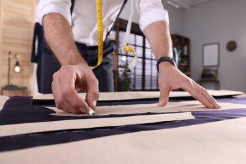 Professional tailor marking sewing pattern on fabric with chalk at table in workshop, closeup