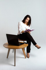 business woman posing while working at her desk. A laptop and some papers were placed in front of her. She is dressed in a strict black suit and talking on the phone. Isolated, white background.