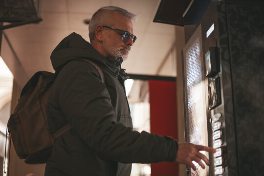 An adult man buys coffee from a vending machine. Automated business.