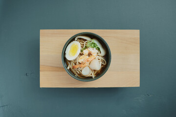 Ceramic bowl of asian ramen soup with shrimp, noodles, spring onion, sliced egg Top view