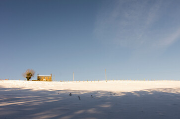 A lone house stands at the top of a snow covered, sunny hill in the North Pennines, Weardale, County Durham
