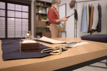 Professional tailor working in atelier, focus on table with scissors and pin cushion. Space for text