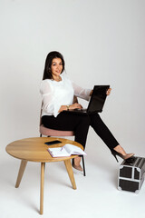 Full length portrait of smiling business woman sitting with laptop and looking at camera on white background