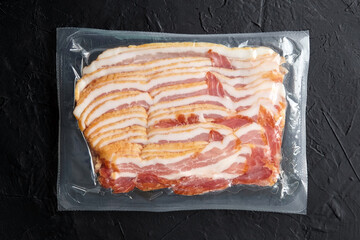 Bacon strips, raw smoked pork meat slices in vacuum package on black table top view