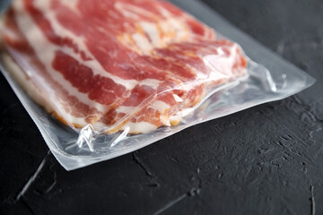 Fototapeta na wymiar Bacon strips, raw smoked pork meat slices in vacuum package on black table