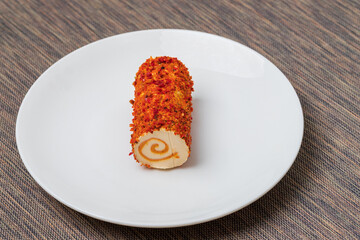 Healthy cheese rolled into a roll wrapped in spices..The cheese is on a white plate.