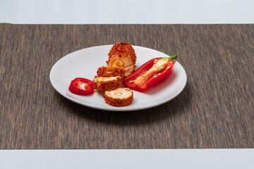 Healthy cheese rolled into a roll wrapped in spices with red pepper..The cheese is on a white plate.