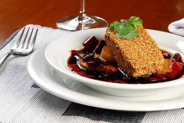 fish fillet covered with sesame in an apple sauce, on a wooden table with a fork and tablecloth