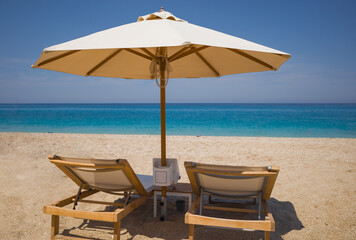 Two wooden sun loungers and sun umbrella on sandy beach with turquoise sea. Holidays without people on islands of Greece