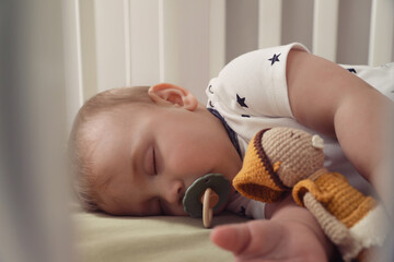 Adorable little baby with pacifier and toy sleeping in crib, closeup