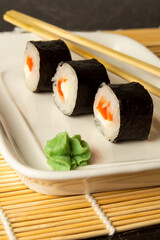 Sushi rolls with salmon lie on a white dish and a bamboo mat on a dark background