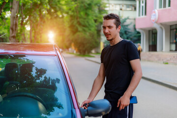 A young man or adult guy driver gets into the car. Background with copy space