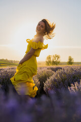 Beautiful and pretty young woman in yellow dress relaxes and enjoys walk in the lavender field at...