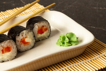 Sushi rolls with salmon lie on a white dish and a bamboo mat on a dark background