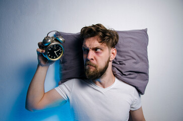 Angry man looking at alarm clock after sleepless night 