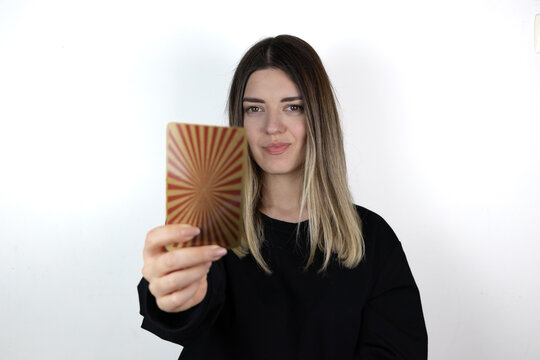 Young woman with casual clothes holding magical card and showing it to the camera. She is so happy and smiling. Tarot card. Photo taken is white isolated background.