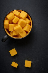 Cubes of sweet ripe mango in sugar in a cup on a dark background