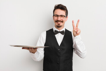 young handsome man smiling and looking happy, gesturing victory or peace. waiter and tray concept