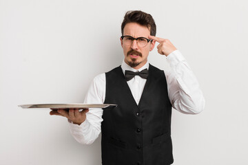 young handsome man feeling confused and puzzled, showing you are insane. waiter and tray concept