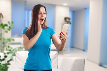Smiling woman at home using smartphone, scrolling through internet on phone.