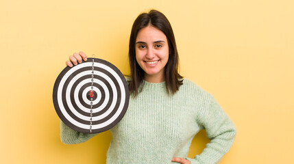 young hispanic woman smiling happily with a hand on hip and confident. darts target concept