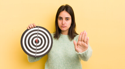 young hispanic woman looking serious showing open palm making stop gesture. darts target concept