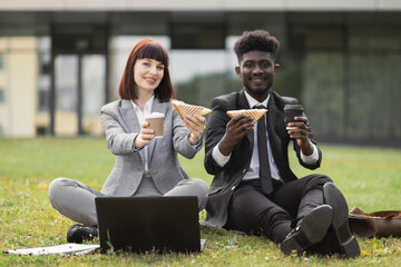 Handsome African-American businessman and his female Caucasian colleague, eating lunch sandwiches...