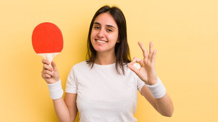 young hispanic woman feeling happy, showing approval with okay gesture. ping pong concept