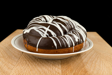 bun covered with chocolate, in a white plate, on a wooden board, on a black background