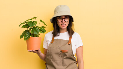 young hispanic woman feeling puzzled and confused. gardener and plant concept