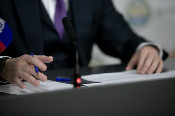 One of politician sitting by table with his hands over document during political summit or conference