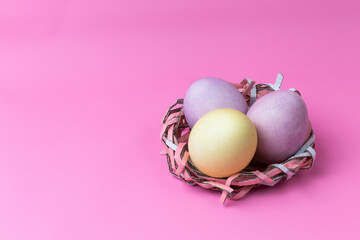 three easter eggs in a homemade nest on a pink background