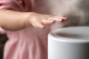 Fototapeta na wymiar A child's hand over the cold steam flowing from the humidifier. Selective focus. Close-up.
