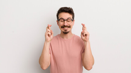 hispanic young man smiling and anxiously crossing both fingers, feeling worried and wishing or...
