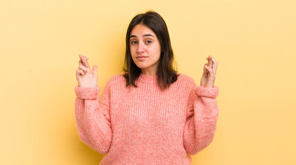 young hispanic woman crossing fingers anxiously and hoping for good luck with a worried look