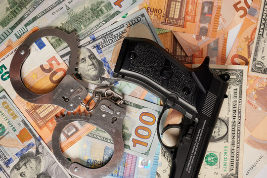 Handcuffs and gun - photo on money bank notes. Jail handcuffs and black gun are laying on money bank notes. Financial background for criminal business. Balance of crime and law. Legal money safety.