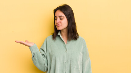 young hispanic woman feeling happy and smiling casually, looking to an object or concept held on...