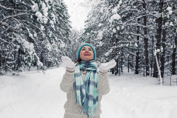 Fototapeta na wymiar A girl stands in the winter forest, cheerfully throws up the snow in white mittens