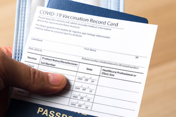 Passport with COVID-19 Vaccination record card and medical mask in hand. Close up view.  - Image