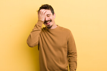 young hispanic man laughing and slapping forehead like saying d’oh! I forgot or that was a stupid...