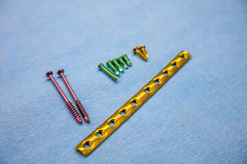  explanted titanium surgical one-third tube plate and titanium screws of different colors lie on a blue support
