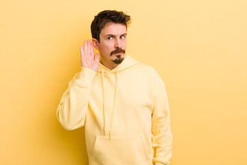 young hispanic man looking serious and curious, listening, trying to hear a secret conversation or...