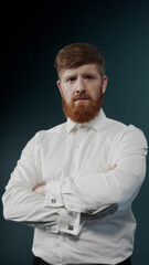 A young guy with red hair and beard shows a serious attitude by crossing his arms on chest