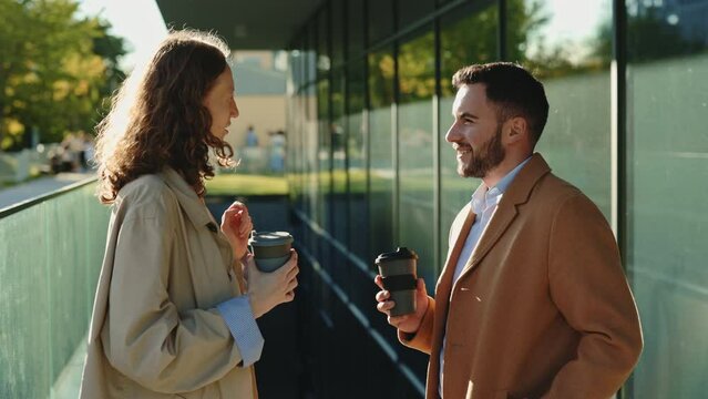 Coworkers with coffee in hands talking near office building