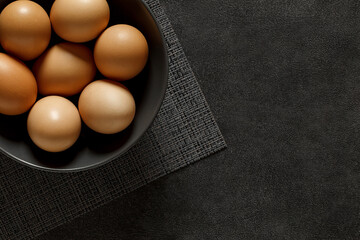 Eggs chicken whole, stacked in gray bowl, on dark background, top view, space to copy text.