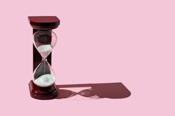 Transparent sand clock with wooden texture. glass hourglass on a pink background.