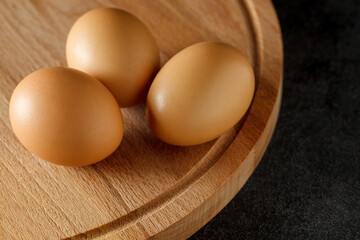 Eggs, three whole, lying on wooden board on dark background, selective focus.
