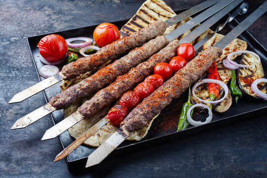 Traditioneller türkischer Adana Kebap am Schaschlik Spieß mit Grillgemüse und Fladenbrot serviert als close-up auf einem rustikalen Metall Tablett