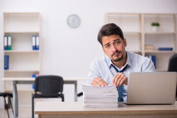 Fototapeta premium Young male employee unhappy with excessive work in the office
