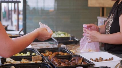 Woman Pays Cash for Food Order to Street Seller. Purchasing fast food in a lunch box on open counters in a cafe. A lot of different ready-fried fish, mushrooms, meat are sold on showcase. Food court.